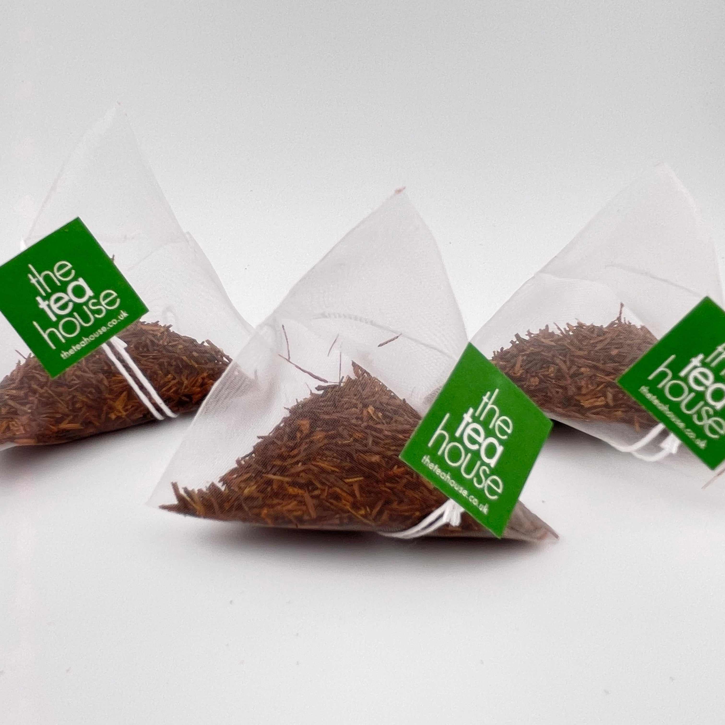 Three triangular tea bags from 'the tea house' on a white background