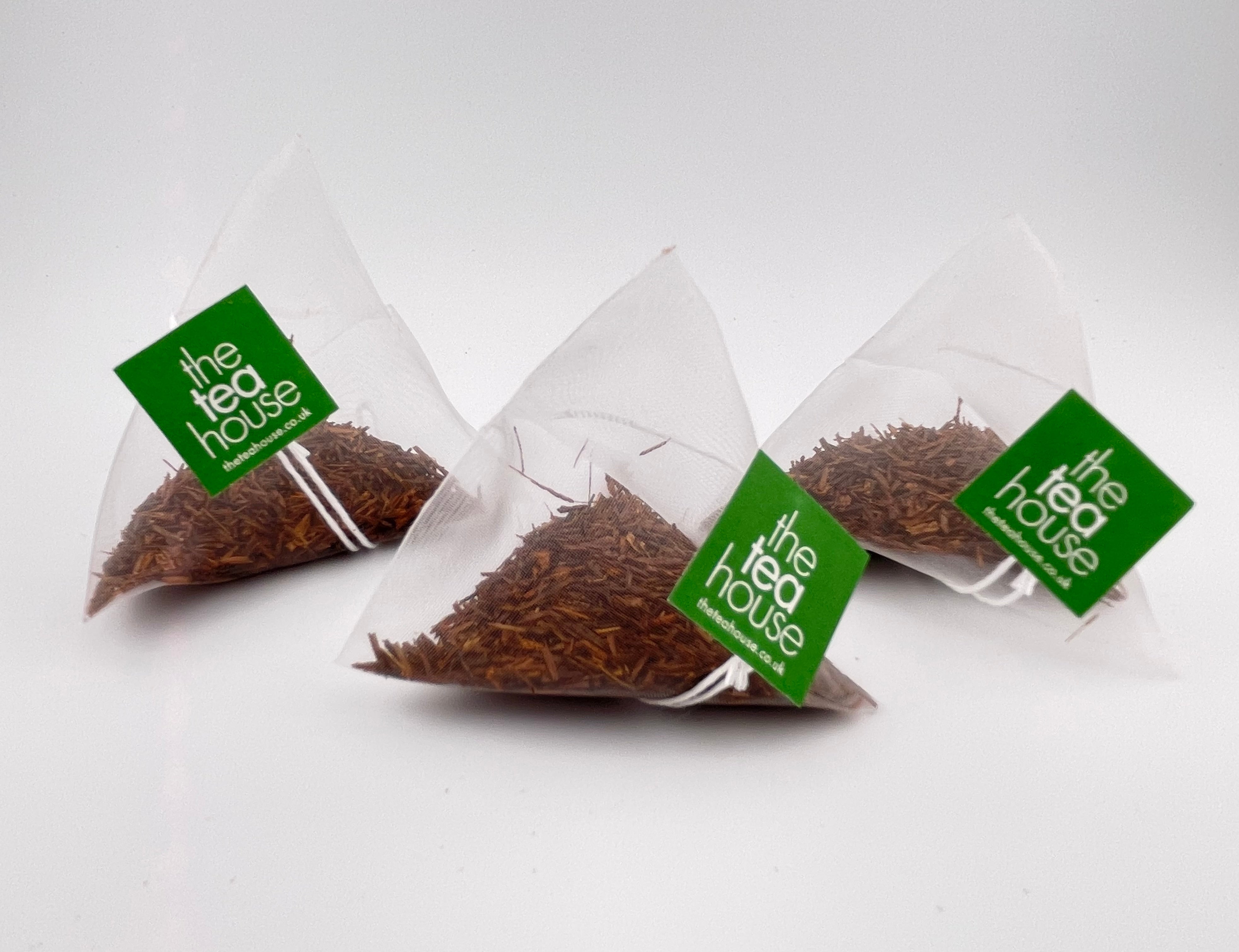 Three triangular tea bags from 'the tea house' on a white background