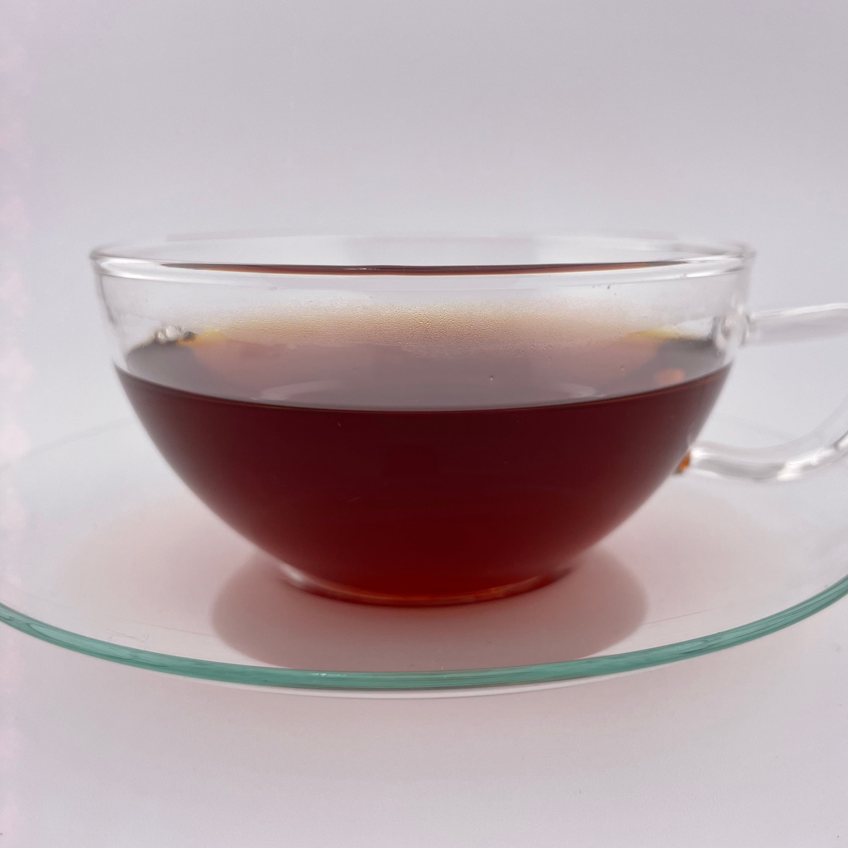 Clear glass cup filled with dark liquid on a matching saucer against a white background
