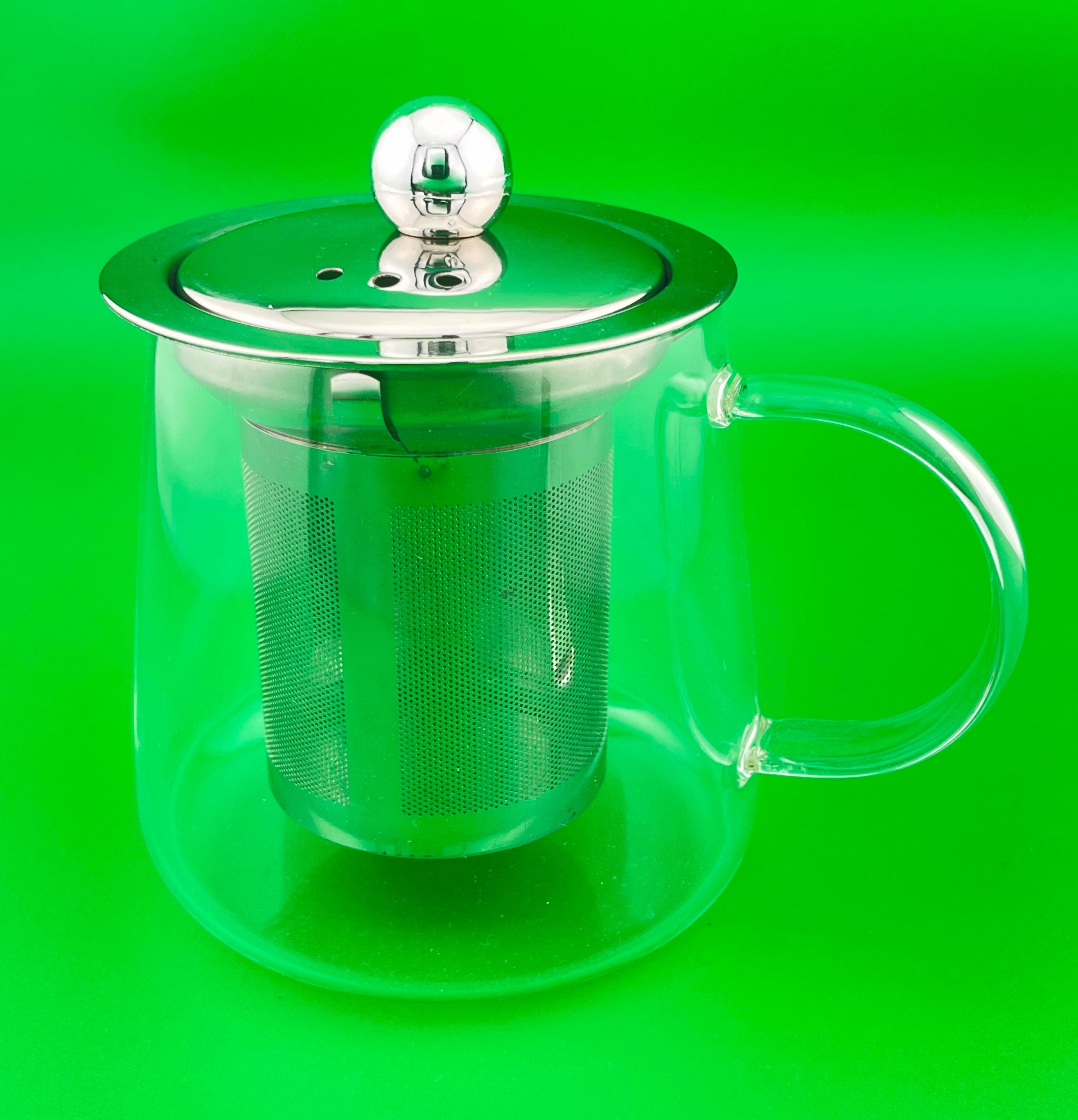 Clear glass teapot with metal mesh lid on a green background