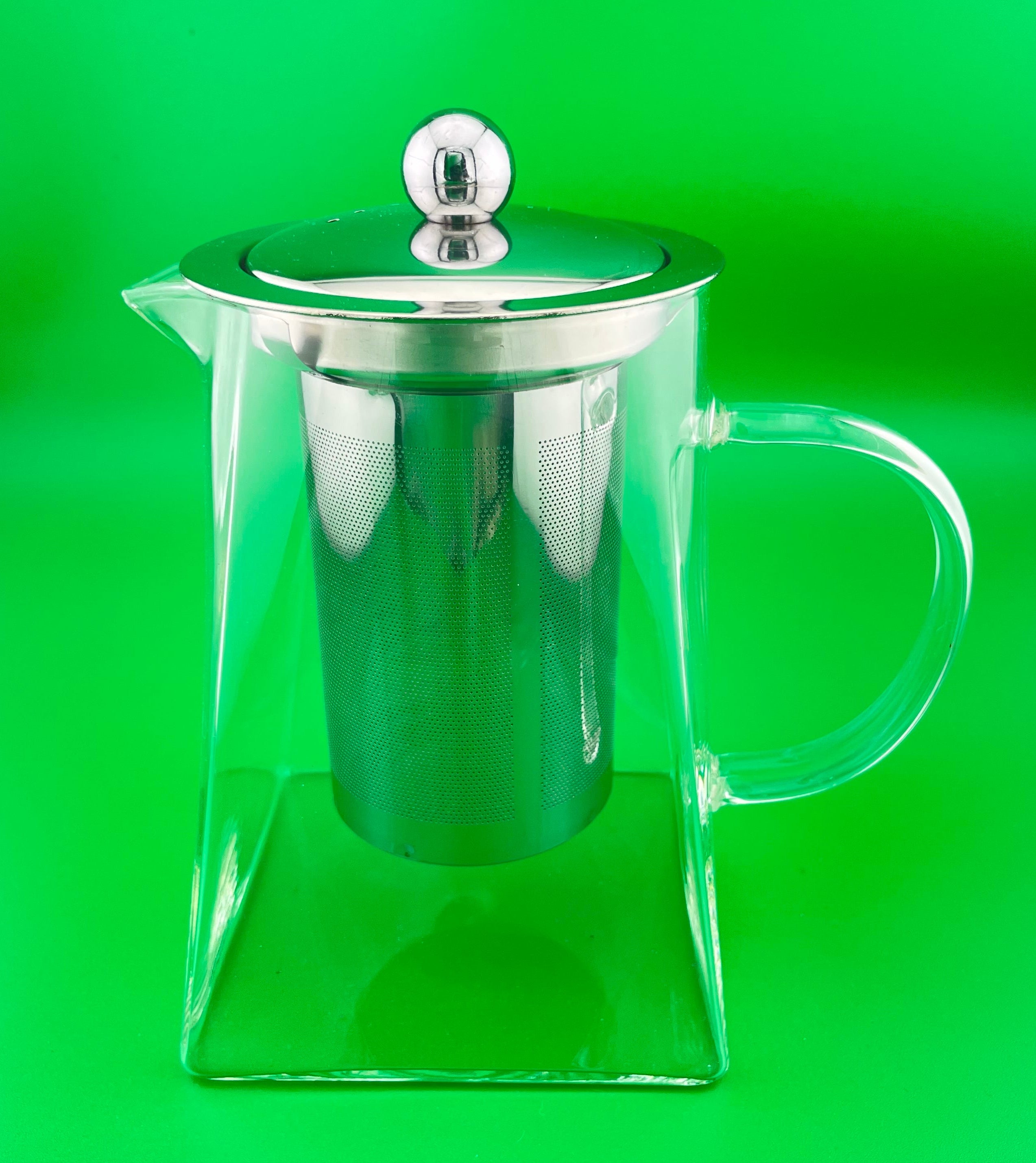 Clear glass teapot with silver lid on a green background