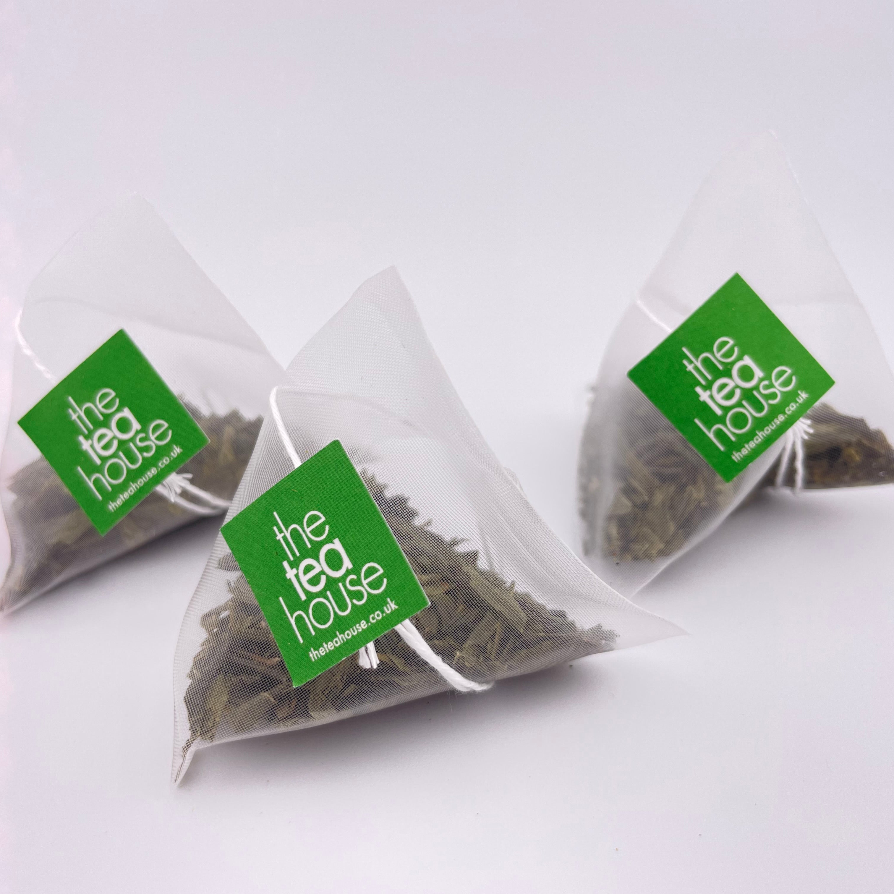 Three triangular tea bags from 'The Tea House' on a white background