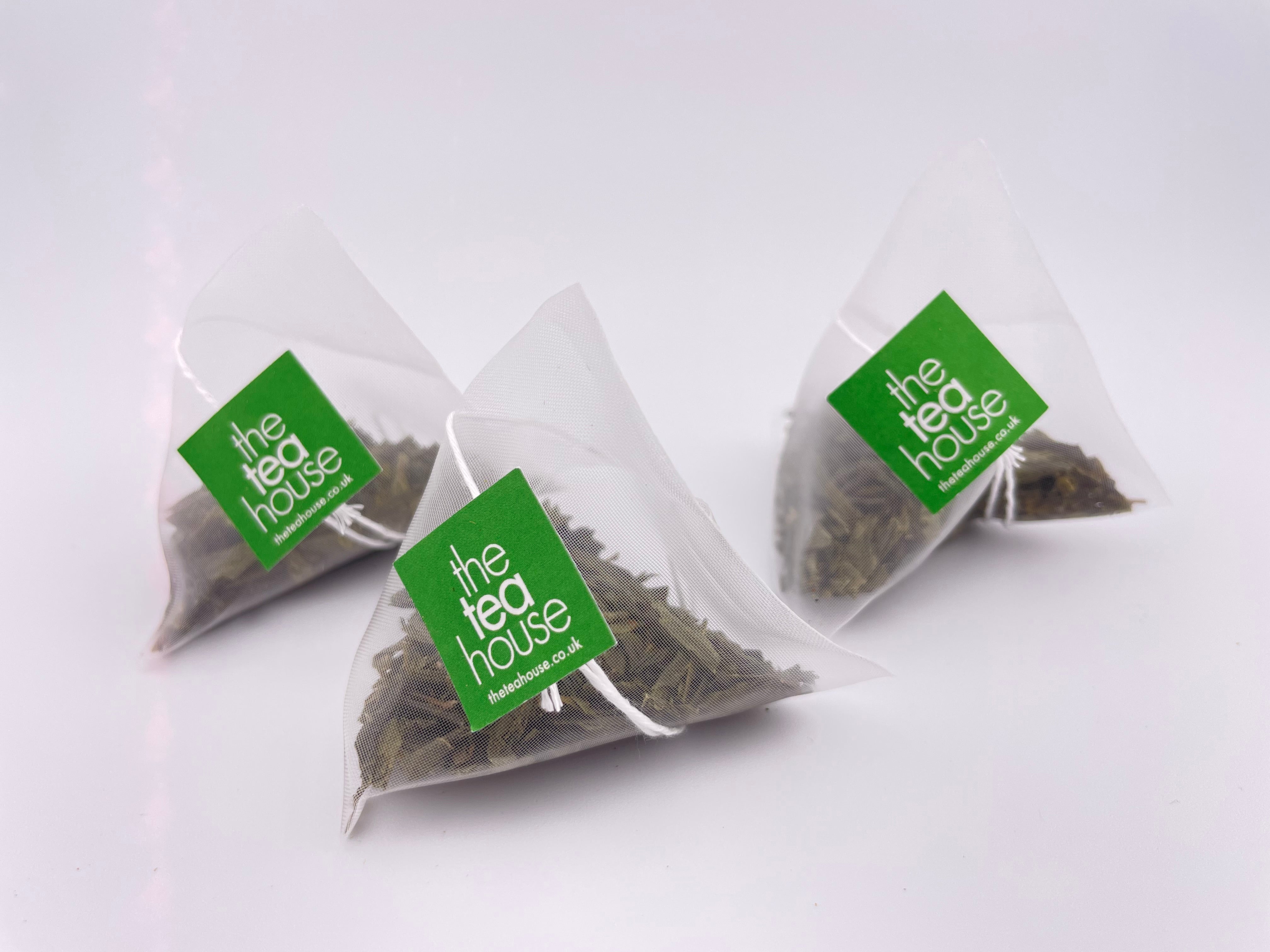 Three triangular tea bags from 'The Tea House' on a white background