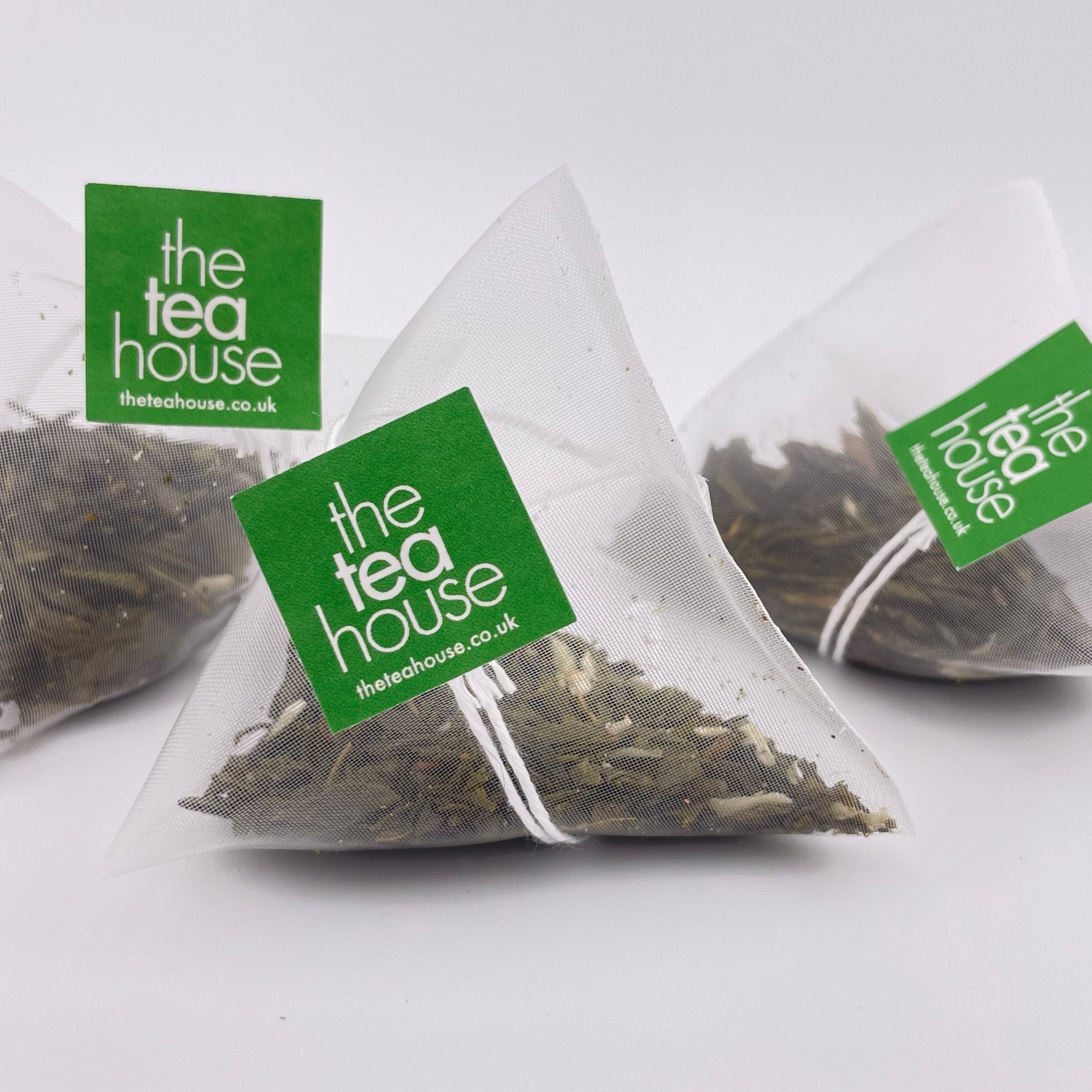 Three triangular tea bags with 'The Tea House' label on a white background