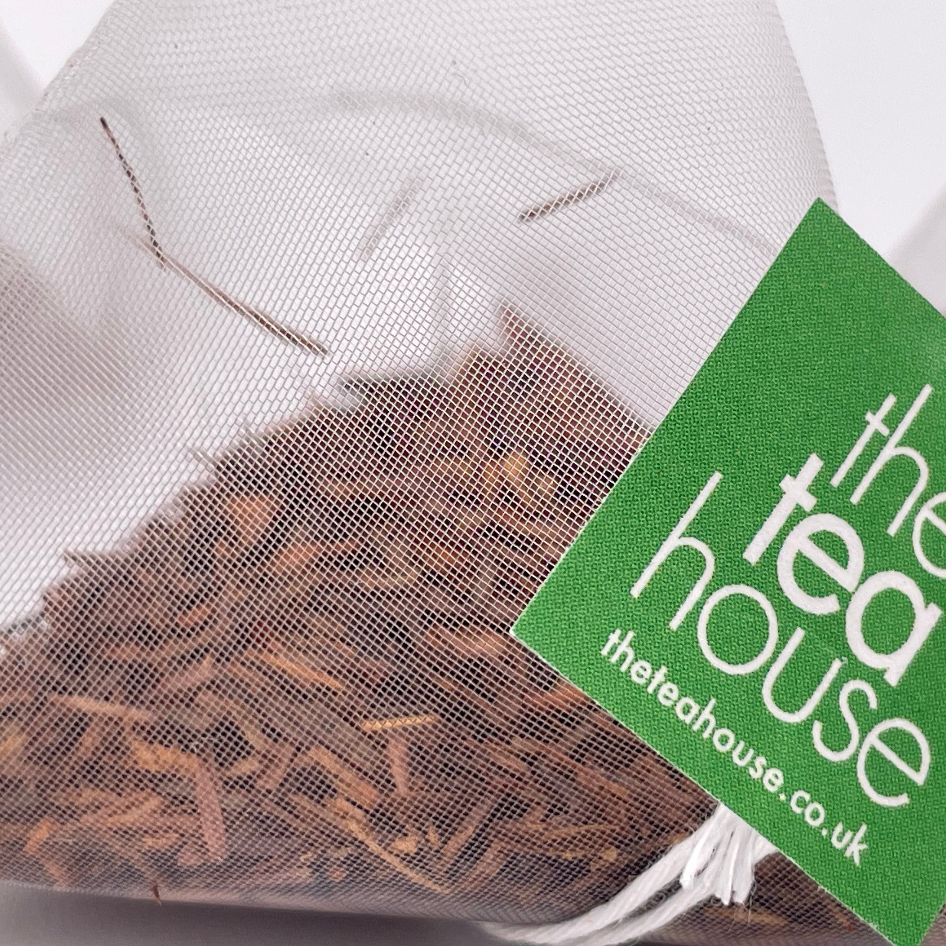 loose leaf rooibos tea leaves in a teabag on white background with green tag "theteahouse"