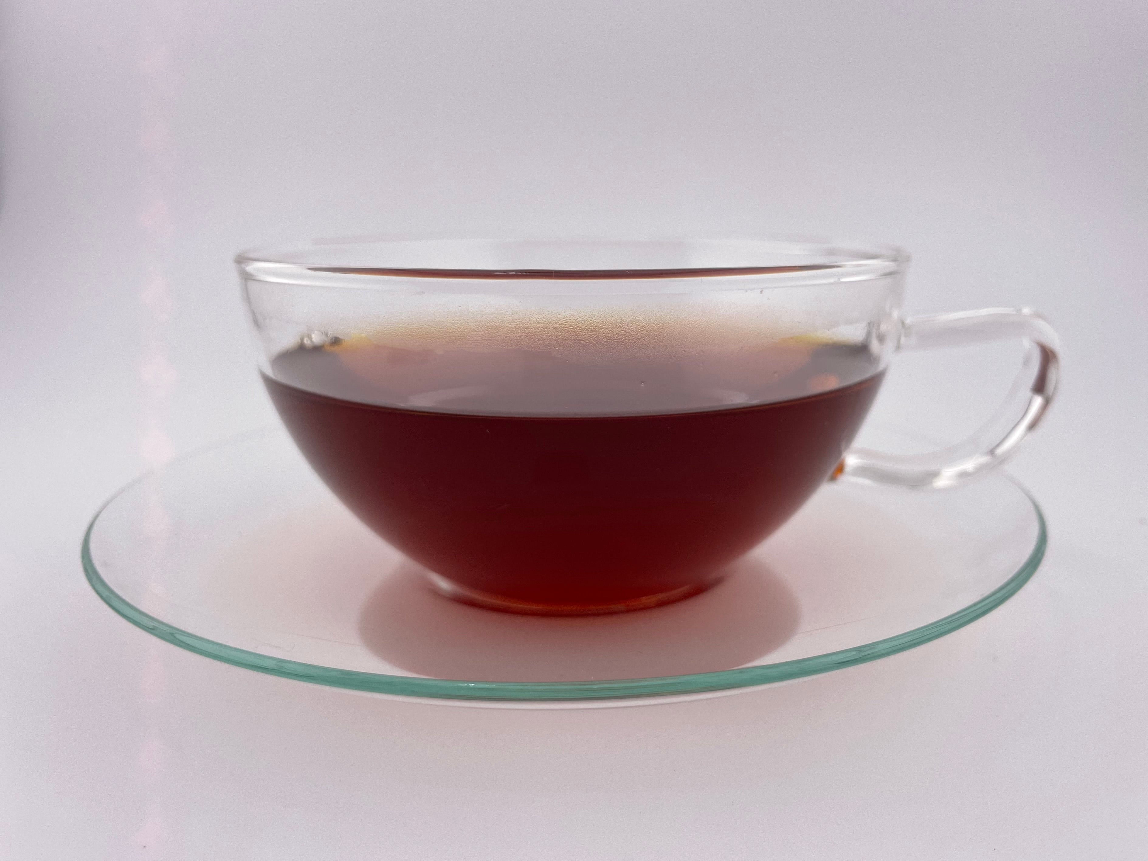 Clear glass cup filled with dark liquid on a matching saucer against a white background