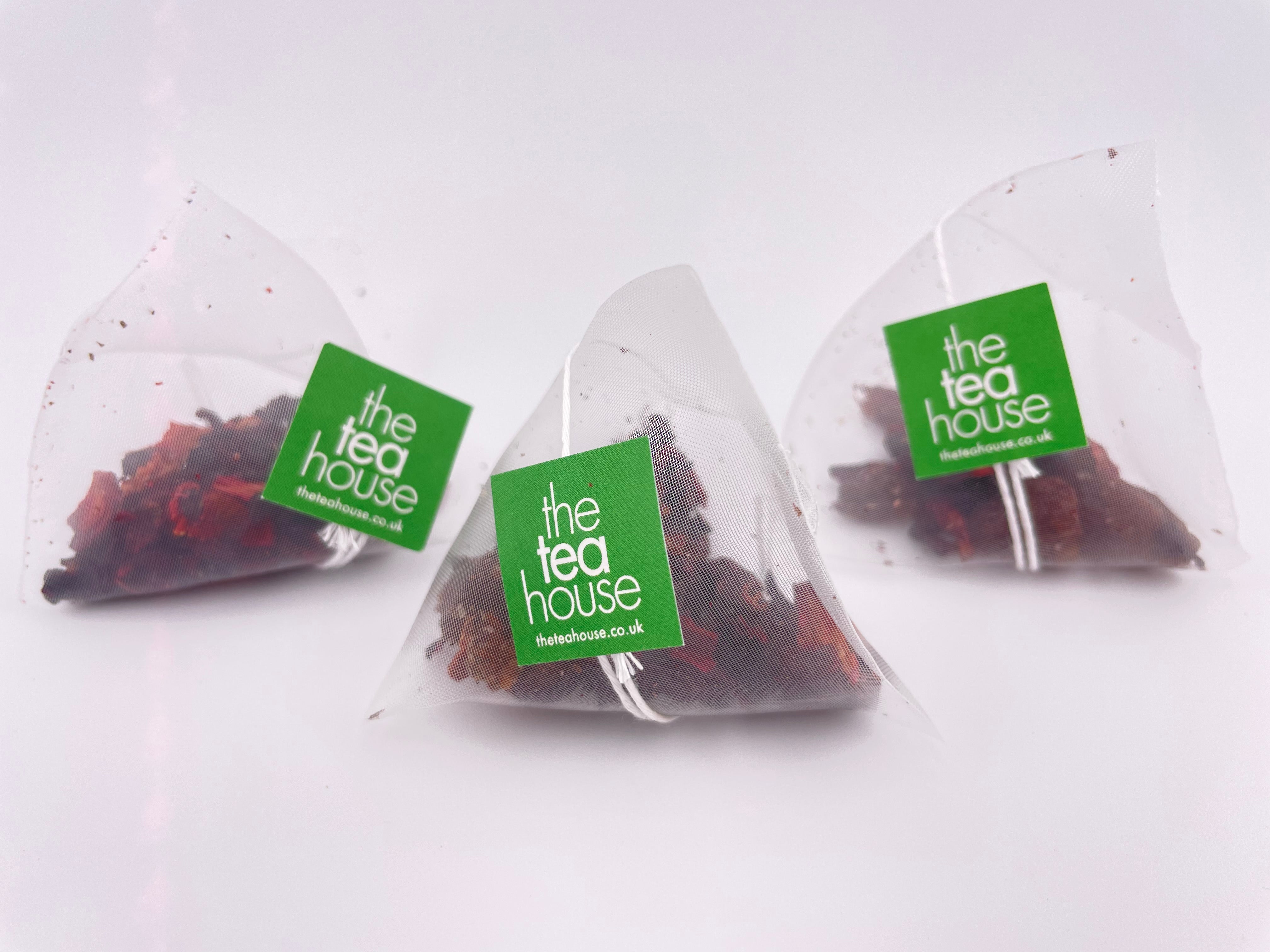 Three transparent tea bags with red and green contents labeled 'the tea house' on a white background.