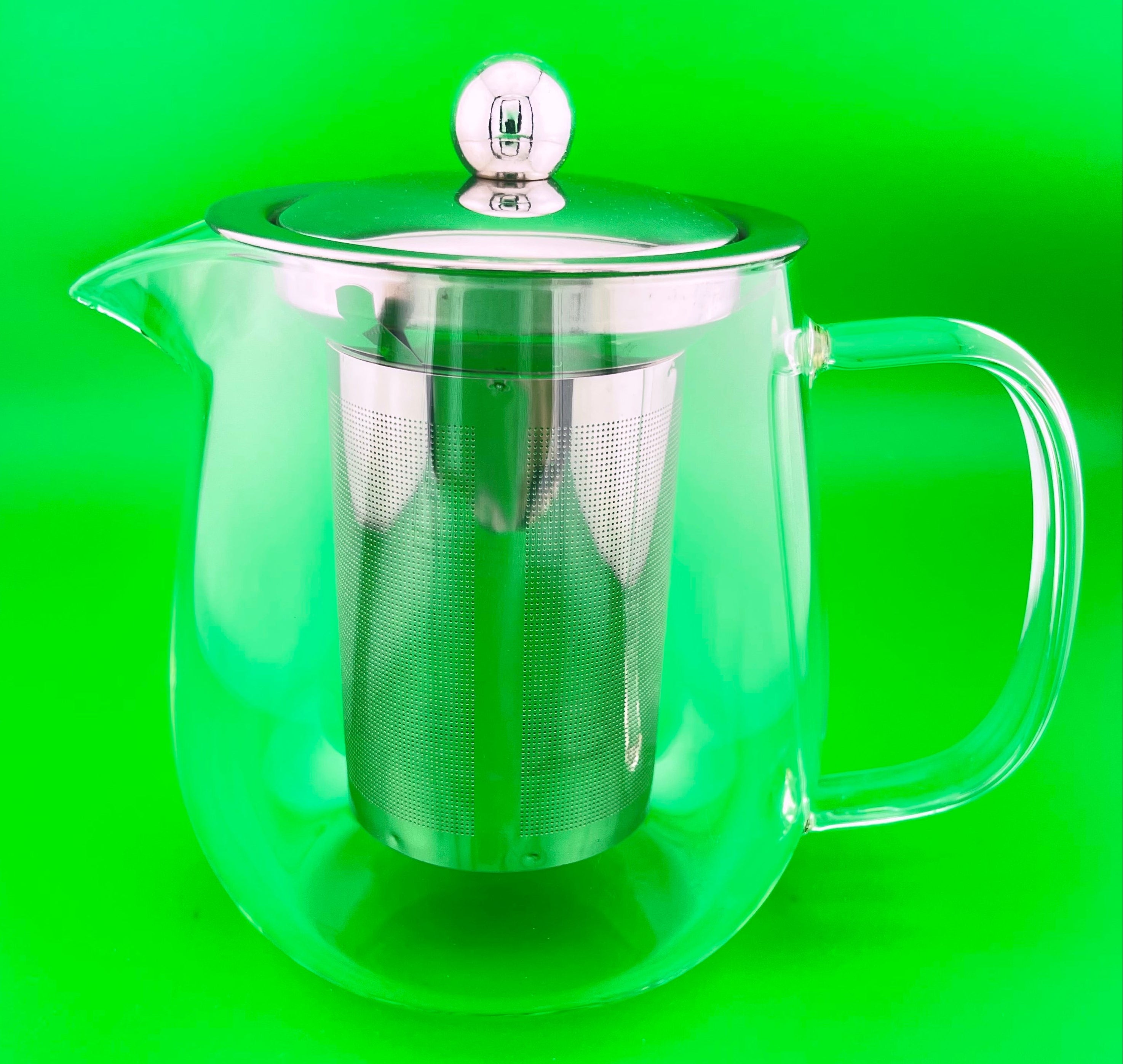 Clear glass teapot with metal handle and infuser on a green background