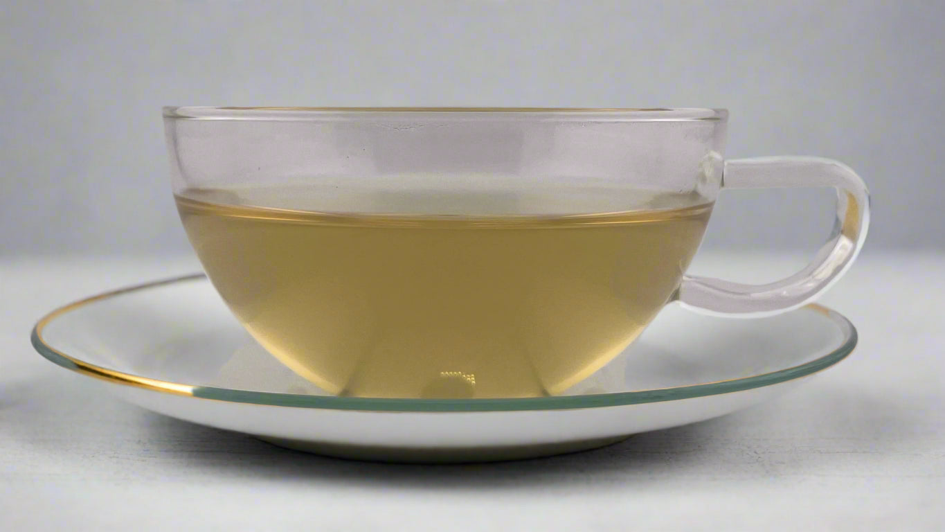 Clear glass teacup with tea on a matching saucer against a plain background