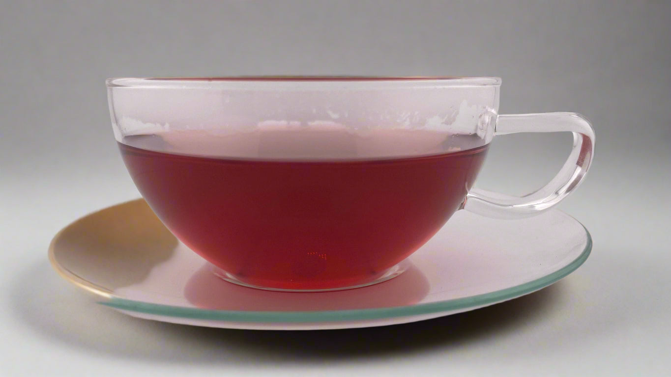 Clear glass teacup with red liquid on a matching saucer against a white background