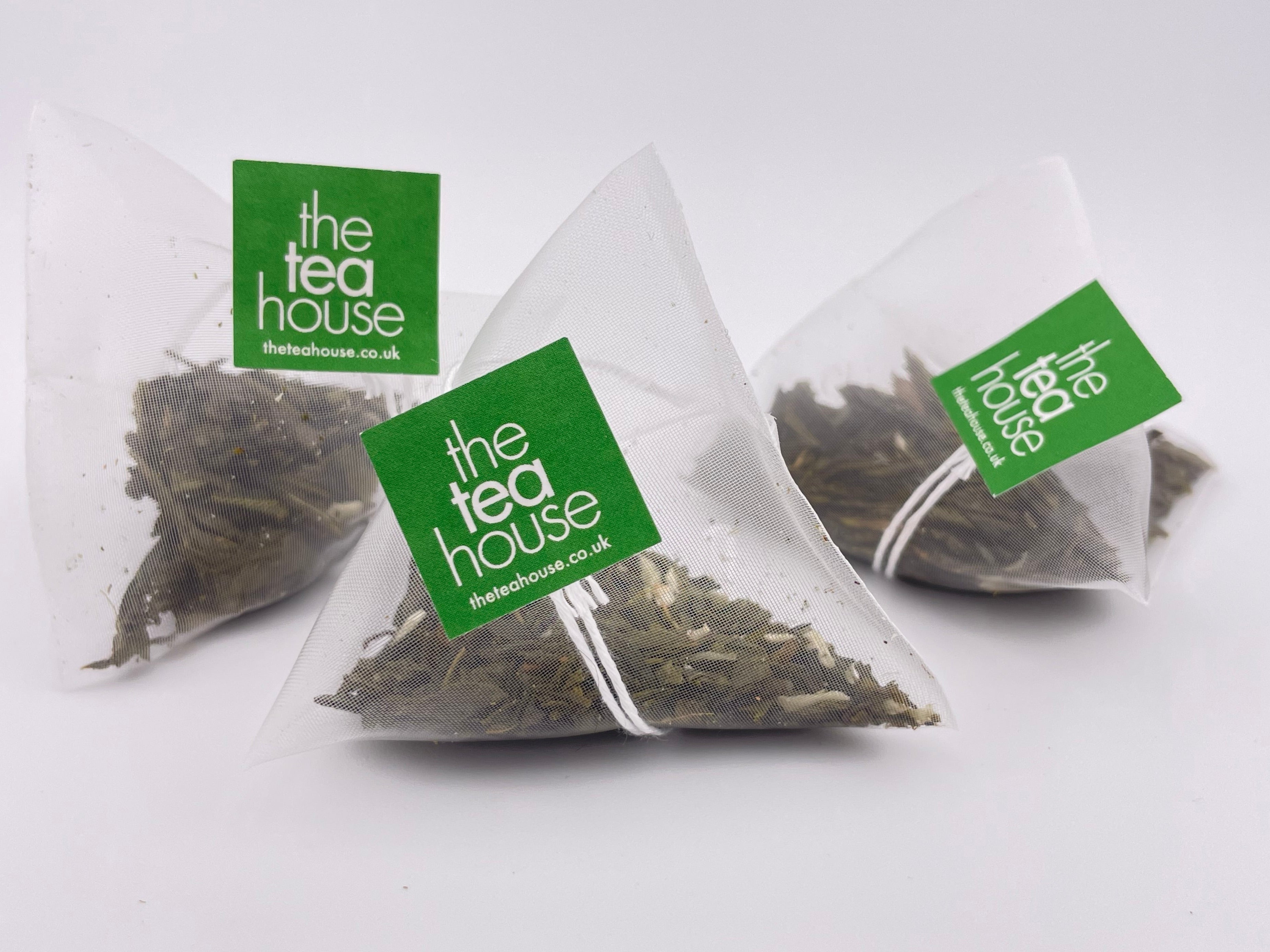 Three triangular tea bags with 'The Tea House' label on a white background