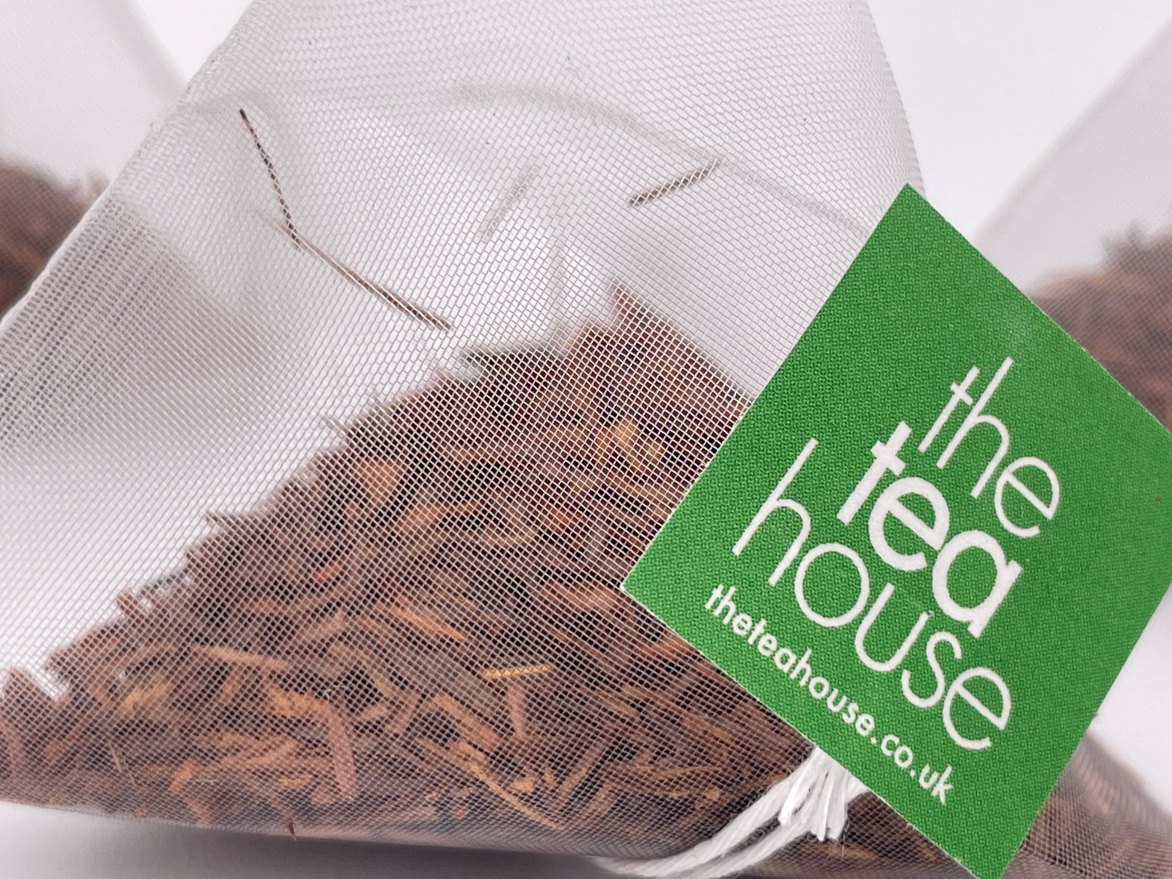 loose leaf rooibos tea leaves in a teabag on white background with green tag "theteahouse"